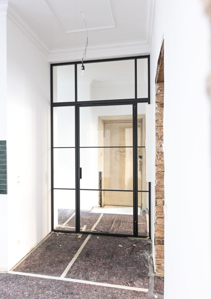 Stahl-Meister Glastrennwand mit Oberlicht, feststehenden Seitenteil und Drehtür, Raumtrenner zwischen Flur, Küche und Wohnzimmer aus Glas in Schwarz, transparentes VSG-Sicherheitsglas, guter Schallschutz, Einbau und Montage in Berlin