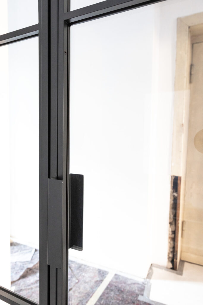 Stahl-Meister Glastrennwand mit Oberlicht, feststehenden Seitenteil und Drehtür, Raumtrenner zwischen Flur, Küche und Wohnzimmer aus Glas in Schwarz, transparentes VSG-Sicherheitsglas, guter Schallschutz, Einbau und Montage in Berlin, Griff, Winkel 40x30x200mm lang