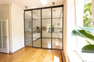 Stahl Loft Tür für Gewerbe und Privat, Windfang als Doppel-Schiebetür mit feststehenden Seitenteilen individuell hergestellt, Aufmaß und Montage in Berlin, maßgeschneiderter Raumtrenner aus Metall und Glas für Loft-Wohnzimmer und Küche