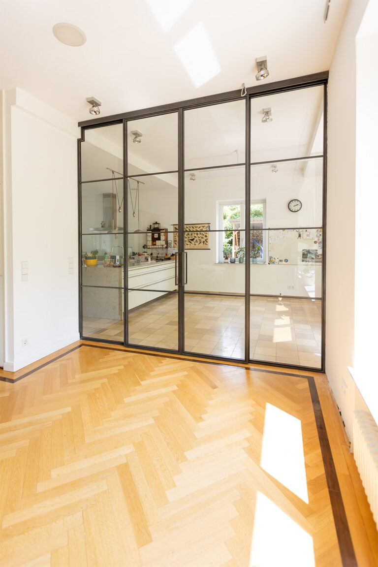Stahl Meister Glastrennwand als Doppel-Schiebetür mit feststehenden Seitenteilen, VSG-Sicherheitsglas für guten Schallschutz, guter Wärmeschutz als Windfang für Küche und Wohnzimmer, Deckenhohe Lofttür aus Stahl und Glas, Aufmaß und Montage, Einbau in Berlin