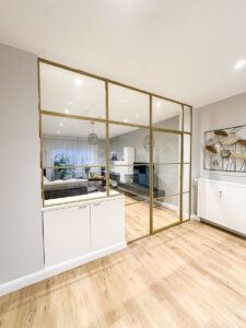 Stahl-Meister Slim Line Loft Tür, Glastrennwand mit goldenem Stahlprofil, Lofttür aus Stahl und Glas, mit Drehtür, Oberlicht und Seitenteil im Wohnzimmer und Küche, Seitenteil auf Schrank befestigt