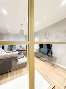 Stahl-Meister Slim Line Loft Tür, Glastrennwand mit goldenem Stahlprofil, Lofttür aus Stahl und Glas, mit Drehtür, Oberlicht und Seitenteil im Wohnzimmer und Küche, Glaskonstruktion, Verbindung von Seitenteilen, aufgesetzte Glassprossen aus Aluminium